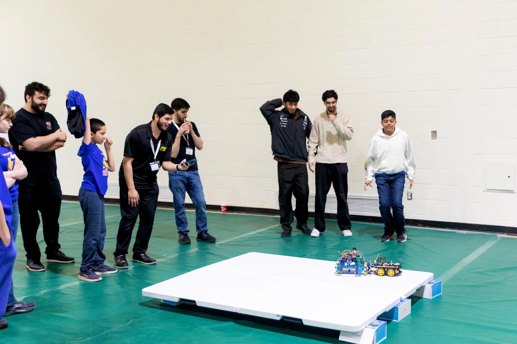 Ahmad refereeing a robot battle at the Genius Cup as students watch